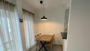 A dining area with a wooden table and chairs, a hanging pendant light, and a view of a cityscape through a window.