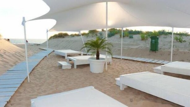A beachside lounge area with white lounge chairs and a canopy providing shade.