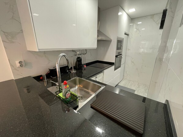 A modern kitchen with a stainless steel sink, black countertop, and white cabinets.