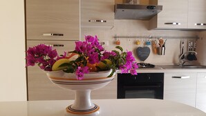 Una cocina con armarios blancos, encimera blanca y un cuenco con flores y fruta.