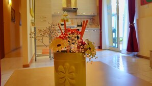 Una habitación con un jarrón amarillo sobre una mesa, una cocina al fondo y una ventana con cortinas.