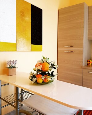 A modern kitchen with a white countertop, a two-tiered fruit and flower arrangement, and wooden cabinets.