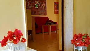 Un vestíbulo de hotel con alfombra roja, una consola blanca con un jarrón de flores rojas y un farol decorativo.