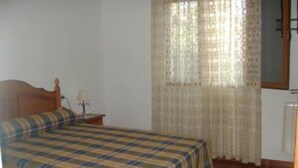 Une chambre à coucher avec un lit, une table de chevet, une lampe et une fenêtre avec des rideaux.