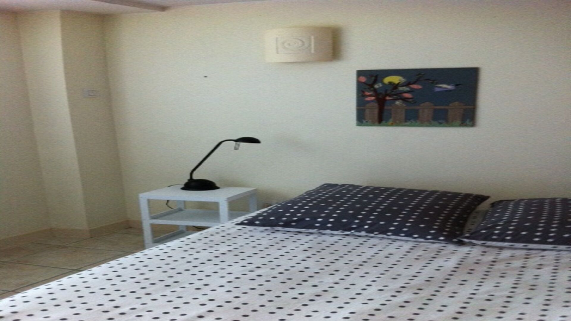 Une chambre à coucher comprenant un lit, une table de chevet, une lampe et un luminaire fixé au mur.