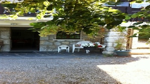 Un bâtiment en pierre avec une allée de gravier, une chaise blanche, une plante en pot et une fenêtre ornée de fleurs.