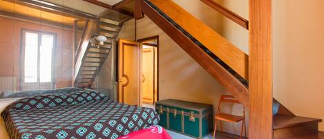 Une chambre à coucher avec un lit, une valise et un escalier en bois.