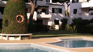A swimming pool with a decorative edge, surrounded by well-maintained lawns and a building with balconies. - Apartment in the solar sector of Dos Pinheiros, Vilamoura (vilamoura)