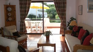 A living room with a sofa, chairs, a coffee table, and a dining area with a table and chairs. There is a wooden cabinet with decorative plates and a potted plant. - Apartment in the solar sector of Dos Pinheiros, Vilamoura (vilamoura)