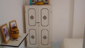 Een witte kast met decoratieve diamantmotieven, een tafeltje met een vaas en een lijst met foto, en een witte stoel.
