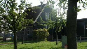 Ein Rasen mit Bäumen, ein Steinhaus und ein Metallzaun.