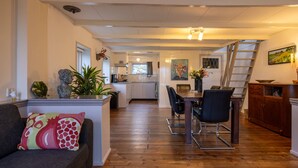 Eine moderne Küche mit weißen Schränken, ein Essbereich mit Holztisch und -stühlen sowie eine Treppe, die zu einer oberen Ebene führt.