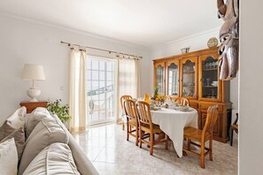 A dining area with a table set for four, a wooden cabinet with glass doors, a sofa, and a lamp.