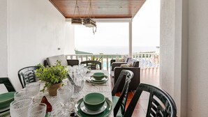 A dining area with a table set for four, chairs, a potted plant, and a view of the sea. - Private villa with sea views, private pool and games room (Ericeira)