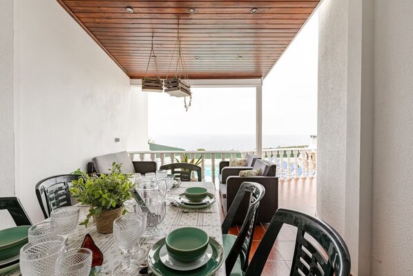 A dining area with a table set for four, chairs, a potted plant, and a view of the sea.