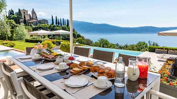 Mesa lista para el desayuno, piscina y una vista panorámica de montañas y agua.