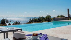 Zona junto a la piscina con una mesa, dos vasos, un cuenco de fruta y vistas al mar.