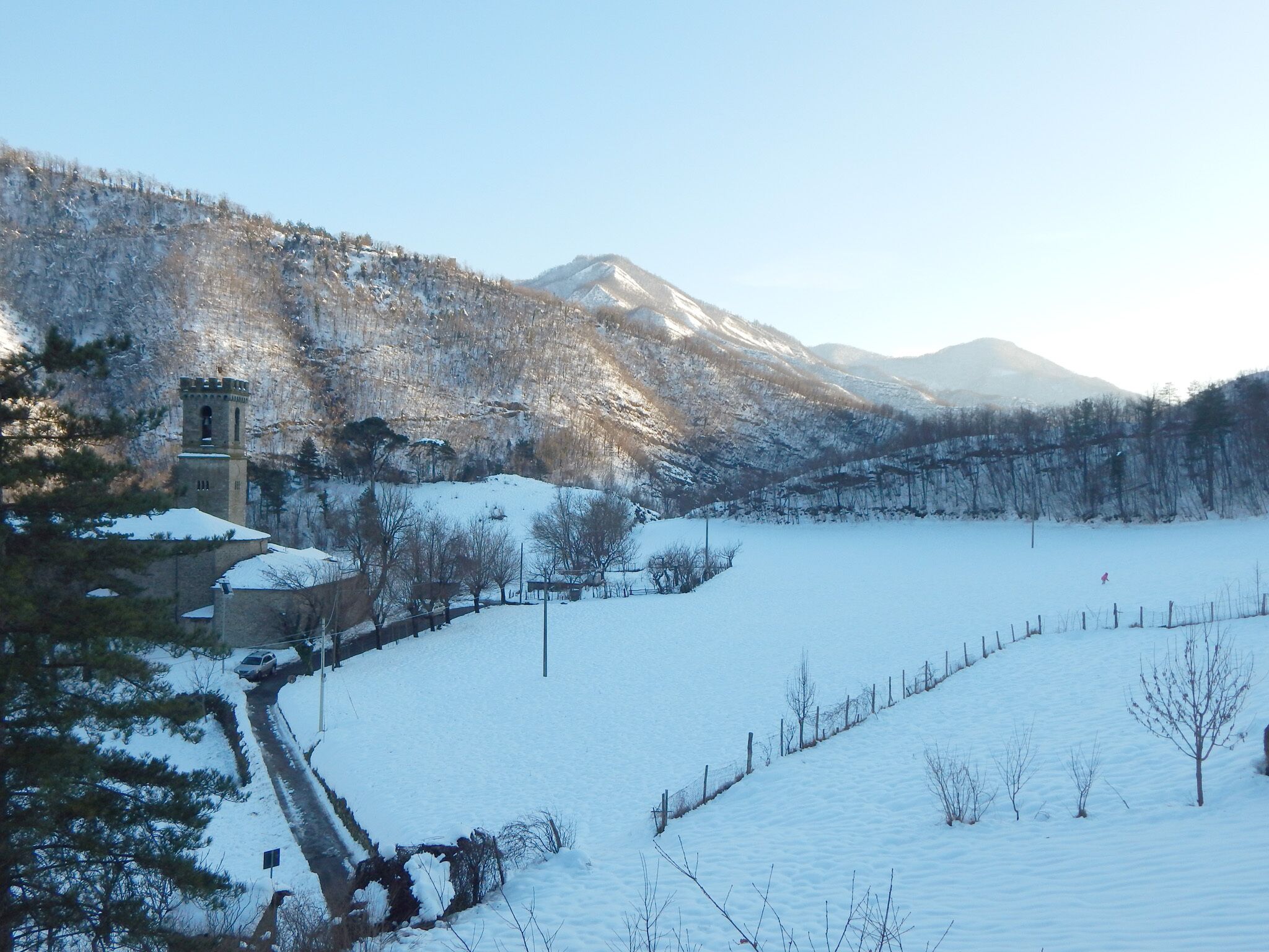 A snow-covered landscape with a tower, a fenced area, and a mountain in the background.
