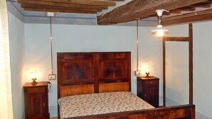 A bedroom with a wooden bed, two bedside tables with lamps, and a wooden ceiling beam. - Giglio: accommodation in an ancient 18th century farmhouse in the Santerno river valley (Firenzuola)