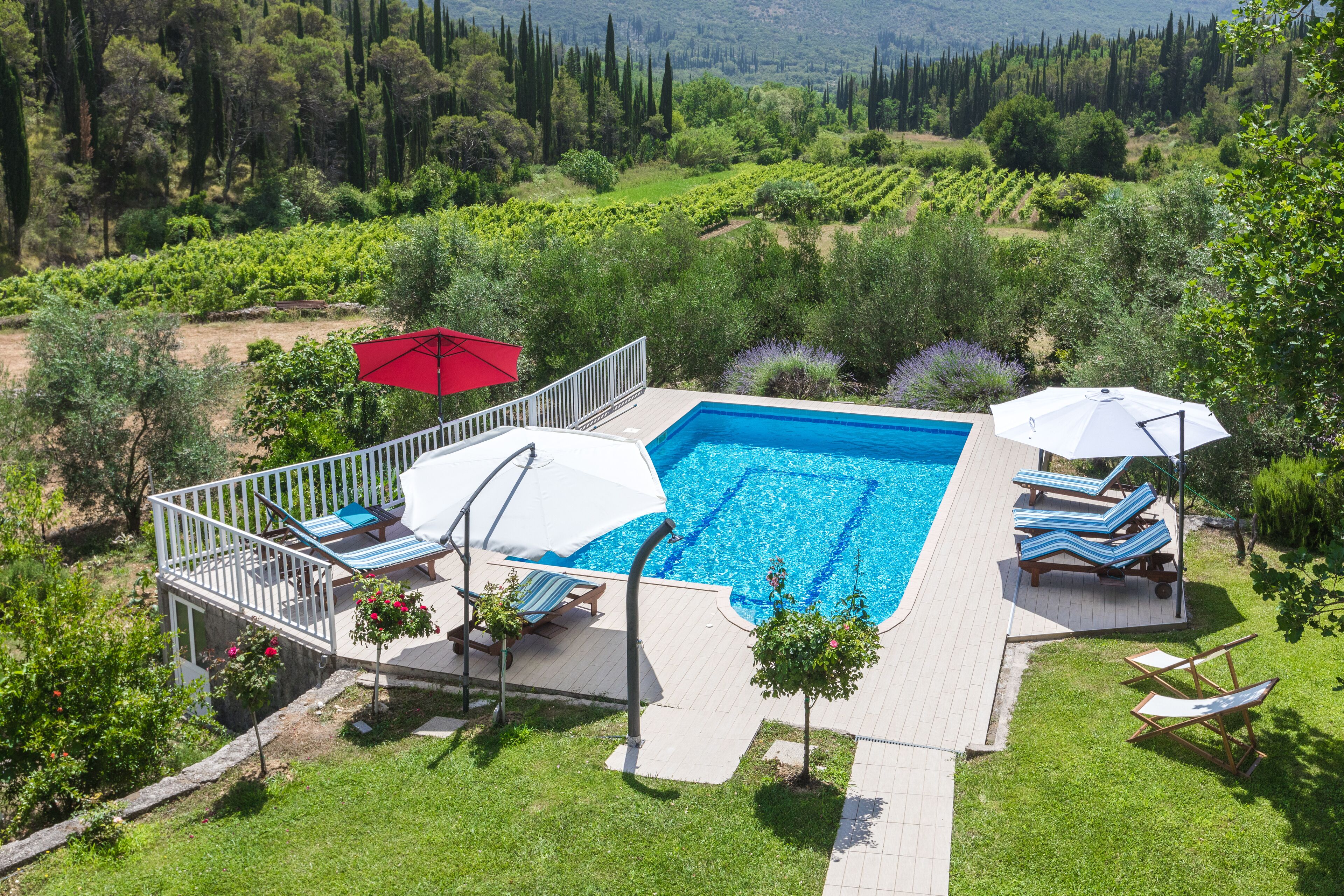 Una piscina con terraza, sillas de descanso y sombrillas.