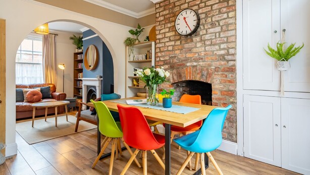 A dining area with a brick wall, a round clock, and a bookshelf. - Buckingham Townhouse -  a family break that sleeps 6 guests in 3 bedrooms (York)