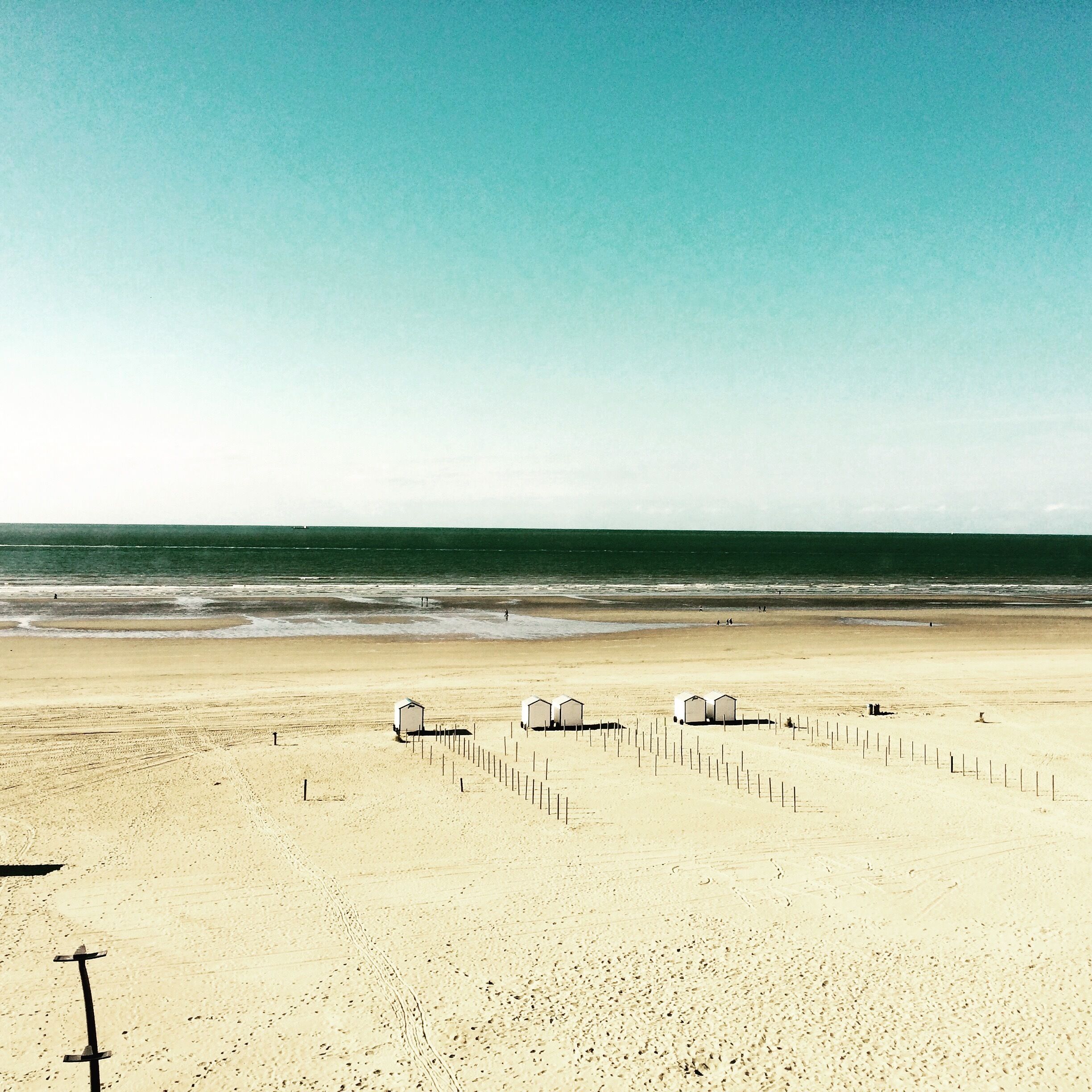 Una platja amb tres cabanes blanques i una tanca.