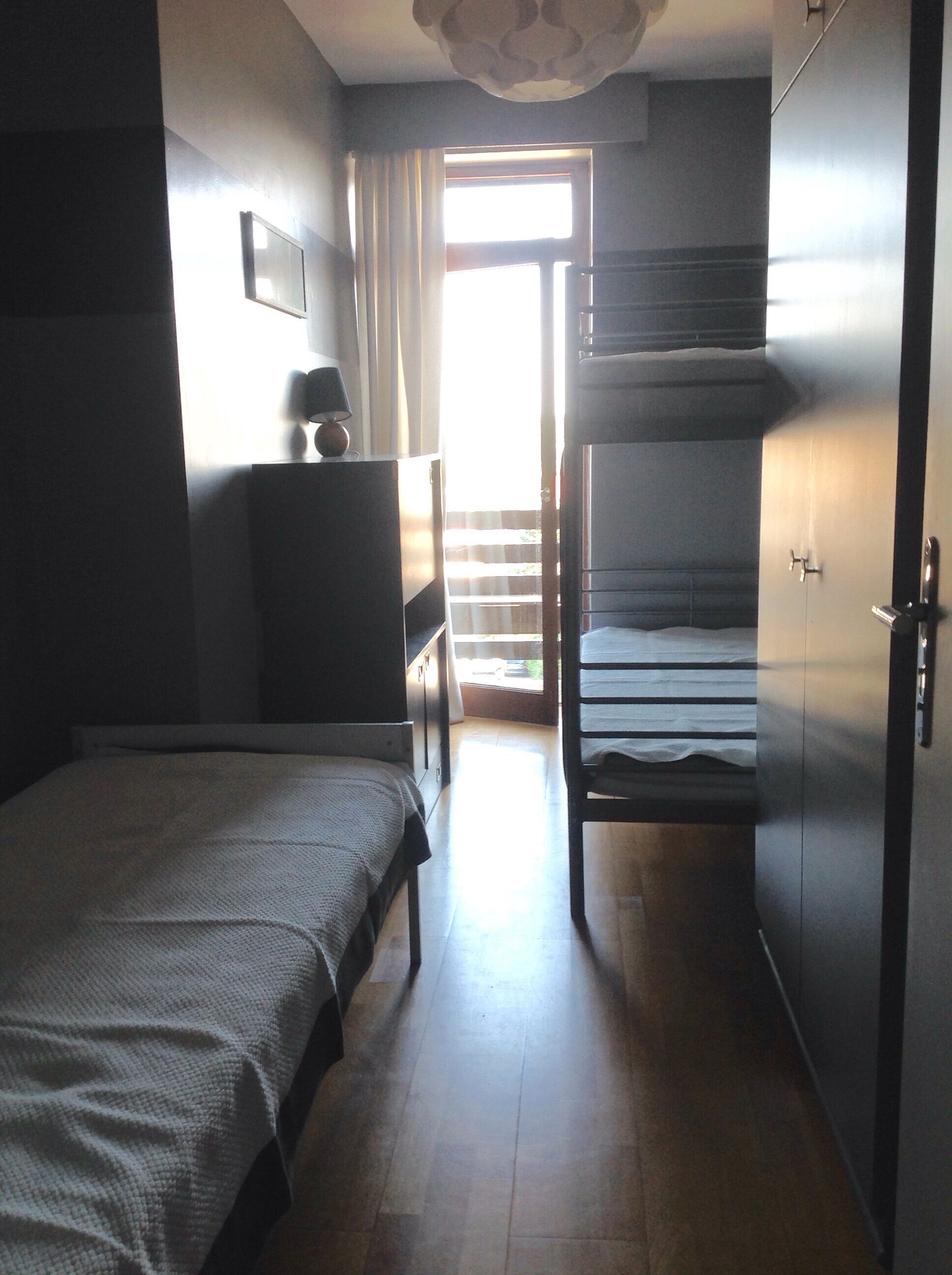A bedroom with a bunk bed, a desk, a lamp, and a window with curtains.