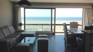Et hotelværelse med stor balkon, sofa, sofabord og skrivebord.