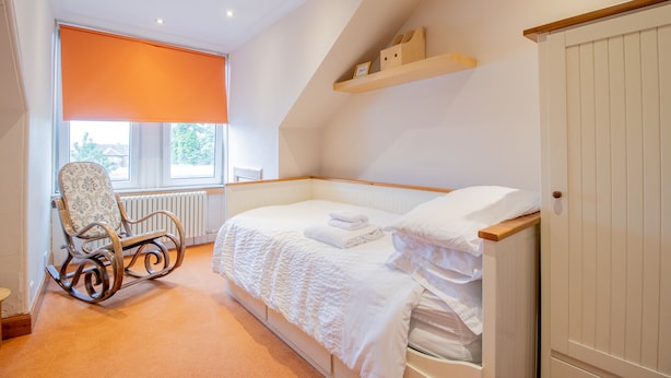 A bedroom with a single bed, a rocking chair, a radiator, and a window with an orange blind. - Comfy Home.  No longer available on this site. No bookings accepted (Hamilton)