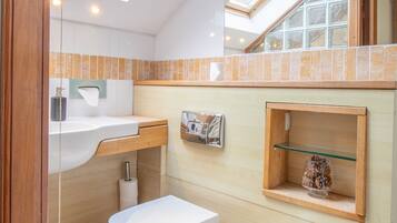 A compact bathroom with a skylight, a bidet, a sink, and a small shelf with decorative items.
