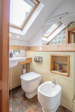 Un bagno compatto con un lucernario, un bidet, un lavandino e un piccolo ripiano con oggetti decorativi.