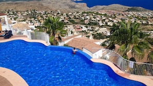 En swimmingpool med utsikt över en kuststad och berg i bakgrunden.