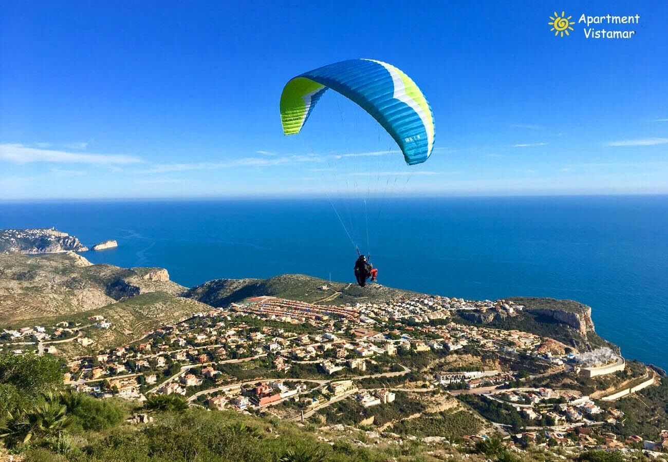 A coastal town with a clear view of the sea and a person paragliding.