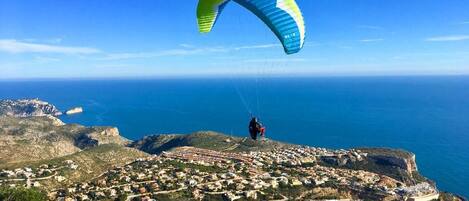 A coastal town with a clear view of the sea and a person paragliding.