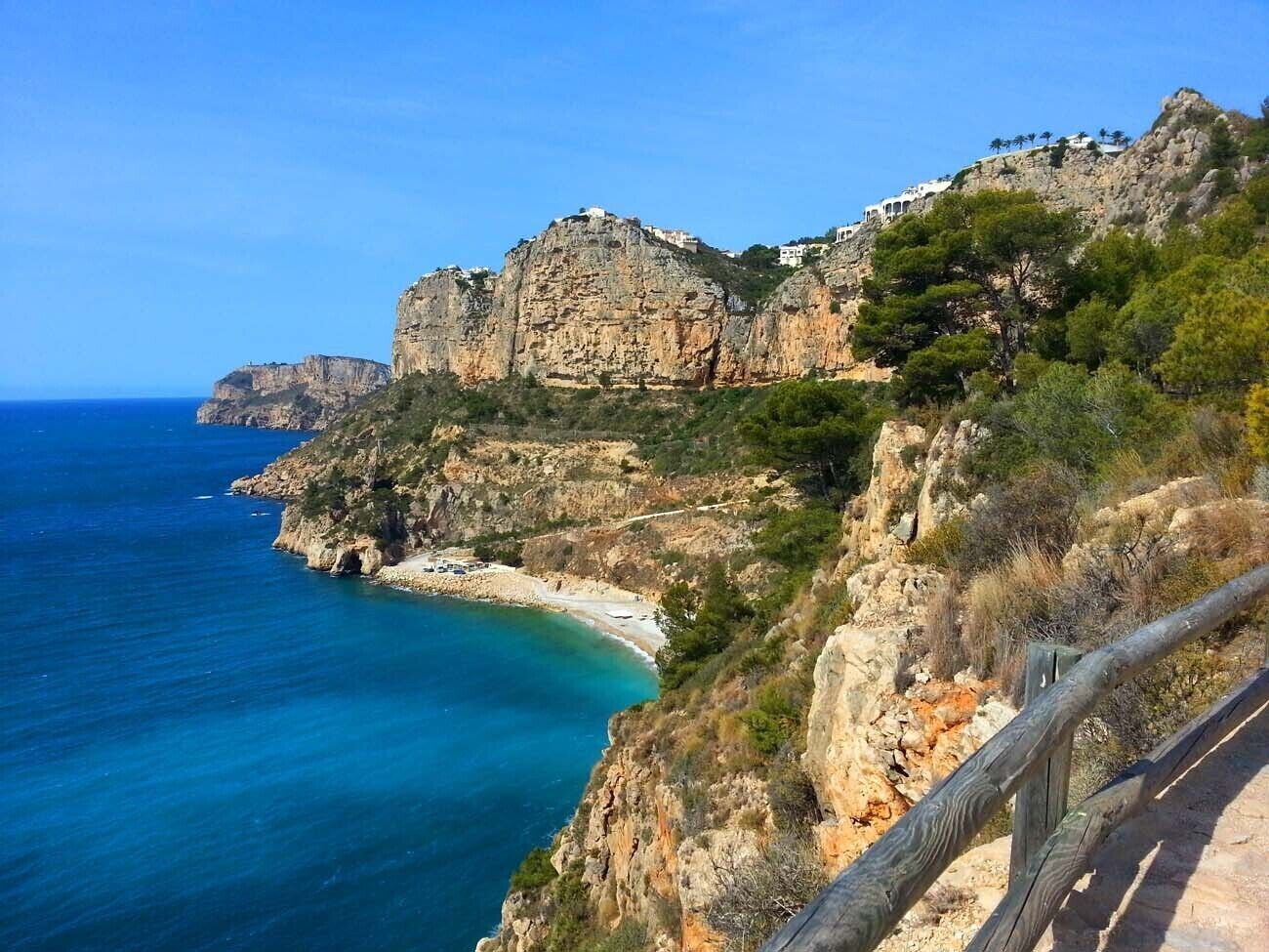 A coastal landscape with rocky cliffs, a beach, and buildings perched on the cliffs.