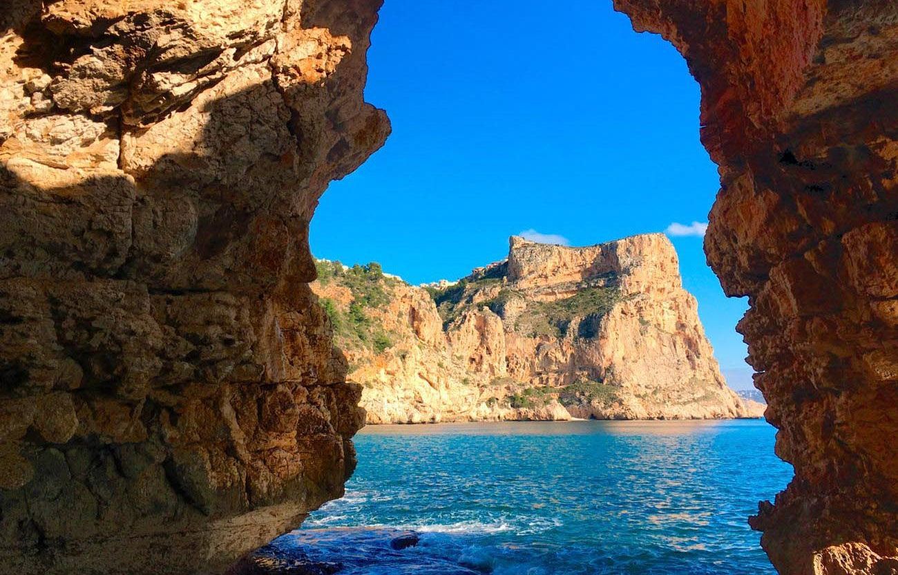 Une vue sur la côte, encadrée par une arche rocheuse naturelle, avec des falaises en arrière-plan.