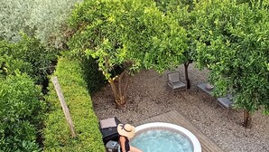 Un bain à remous entouré d’arbustes et d’arbres aux formes soignées, agrémenté de mobilier d’extérieur et d’un chemin en pierre.