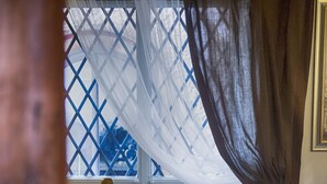 Une chambre à coucher avec un lit, une fenêtre ornée d’un treillis bleu et un rideau.