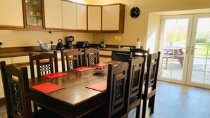 Een eetgedeelte met een houten tafel en stoelen, een keuken op de achtergrond en uitzicht op het buitenlandschap door een glazen deur.