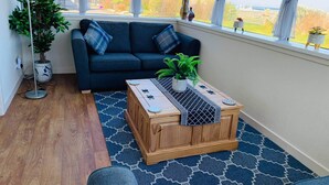 Een gezellige woonkamer met een donkerblauwe bank, een houten salontafel en een groot raam met gordijnen.