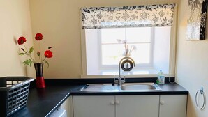 Een kleine keuken met een wasmachine, een spoelbak en een raam met bloemenversiering.