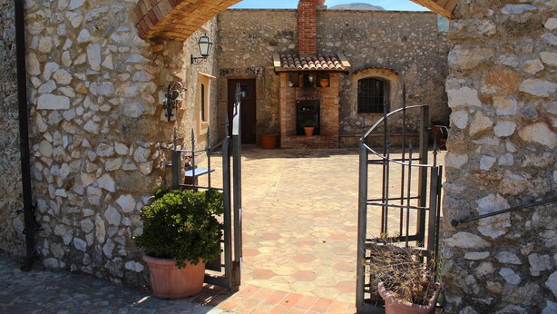 A stone courtyard with an archway leading to a building with a tiled roof and a chimney. There are potted plants and a metal gate. - BEAUTIFUL VILLA with SWIMMING POOL for EXCLUSIVE use, relax a few km from the sea! (Carini)
