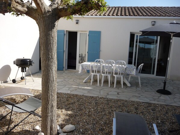 A patio with a table and chairs, a grill, and a tree.