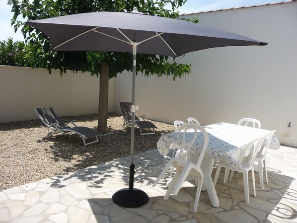 An outdoor patio area with a table and chairs, a large umbrella, and a tree providing shade.