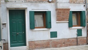 A building with a green door and shutters, a brick base, and a tiled ground. - new renovated apartment 3 rooms - 2/5 persons, modern and well furnished. 8 minuts walk to S. Marco - (Venezia)