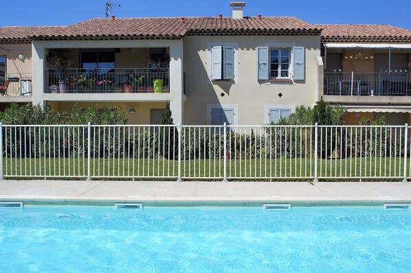 A two-story building with balconies, a swimming pool, and a white fence.