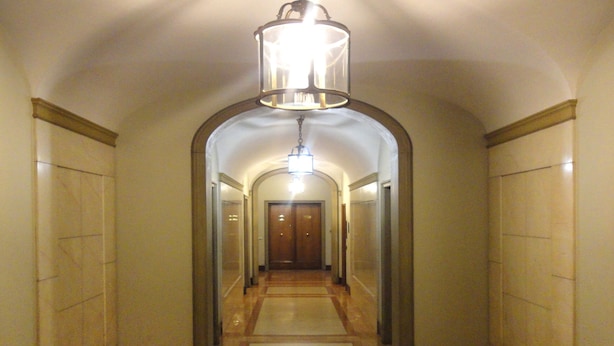 En hall med en central taklampa, speglade väggar och ett trägolv.