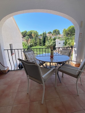 A round table with four chairs, a bottle of champagne, and a glass on a balcony with a view of greenery and buildings.