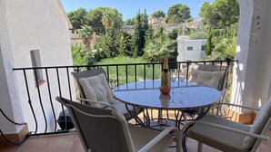 Een ronde tafel met vier stoelen, een champagnefles en een glas op een balkon met uitzicht op groen en gebouwen.