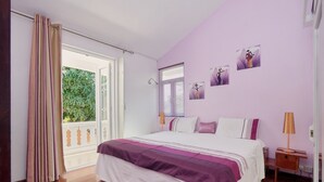 Ein Schlafzimmer mit Bett, Holzboden, einem Fenster mit Jalousien, einem Nachttisch und einer Lampe.